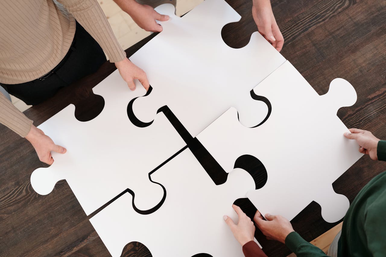 Four people collaboratively putting together oversized puzzle pieces, symbolizing teamwork in an online course design support process.